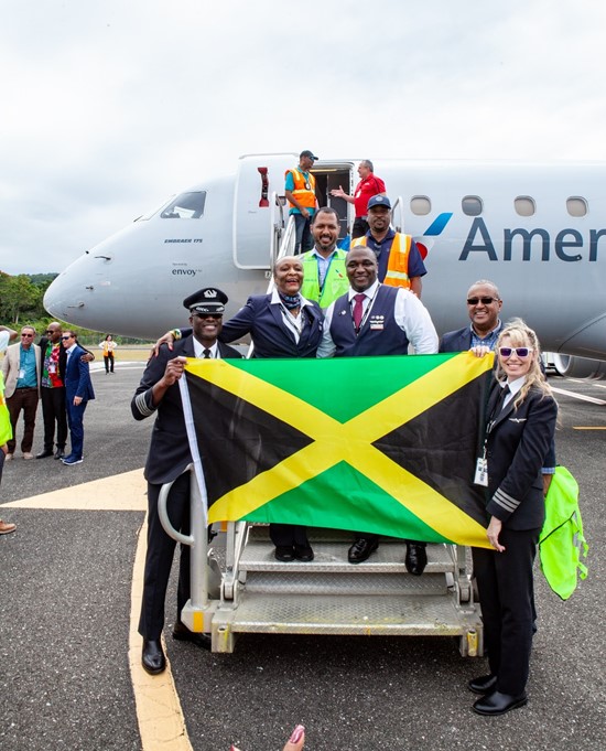 American Airlines pilot Marc Coley (right) waves the Jamaica flag soon after the inaugural flight’s landing at Ian Fleming International Airport from Miami International Airport, while an officer(left) waves to attendees on hand to welcome the plane.