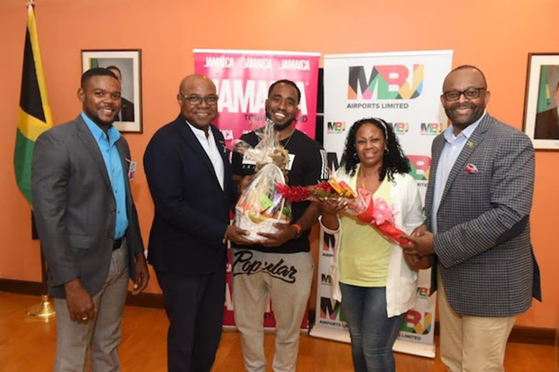 Deputy Mayor, Montego Bay, Richard Vernon (at left); Minister of Tourism, Jamaica, the Hon. Edmund Bartlett (second from left); and Director of Tourism, Jamaica Tourist Board, Donovan White; present gifts to Jamaica’s one millionth stopover visitor Brian Simmons (center) and Brian’s mother and traveling companion, Monica Simmons (second from right) upon their entry into Montego Bay’s Sangster International Airport on June 15, 2022.  